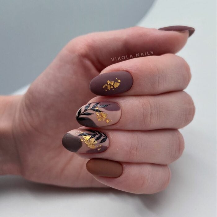 hand showing acrylic nails in strong tones with flower decoration with a little gold leaf 