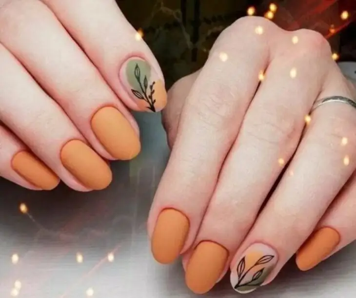 hands of a girl with orange nails with a drawing of a leaf 