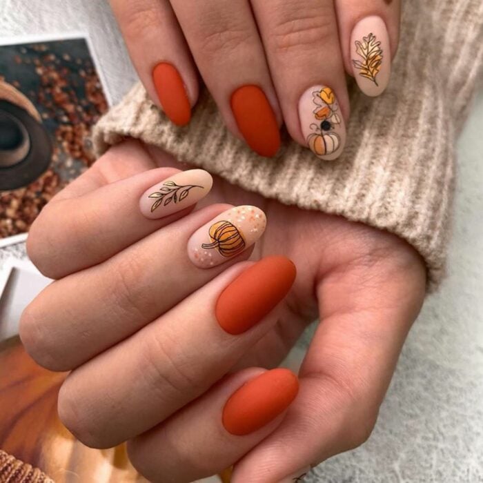 hands showing an orange nail design with figures of leaves and pumpkin 